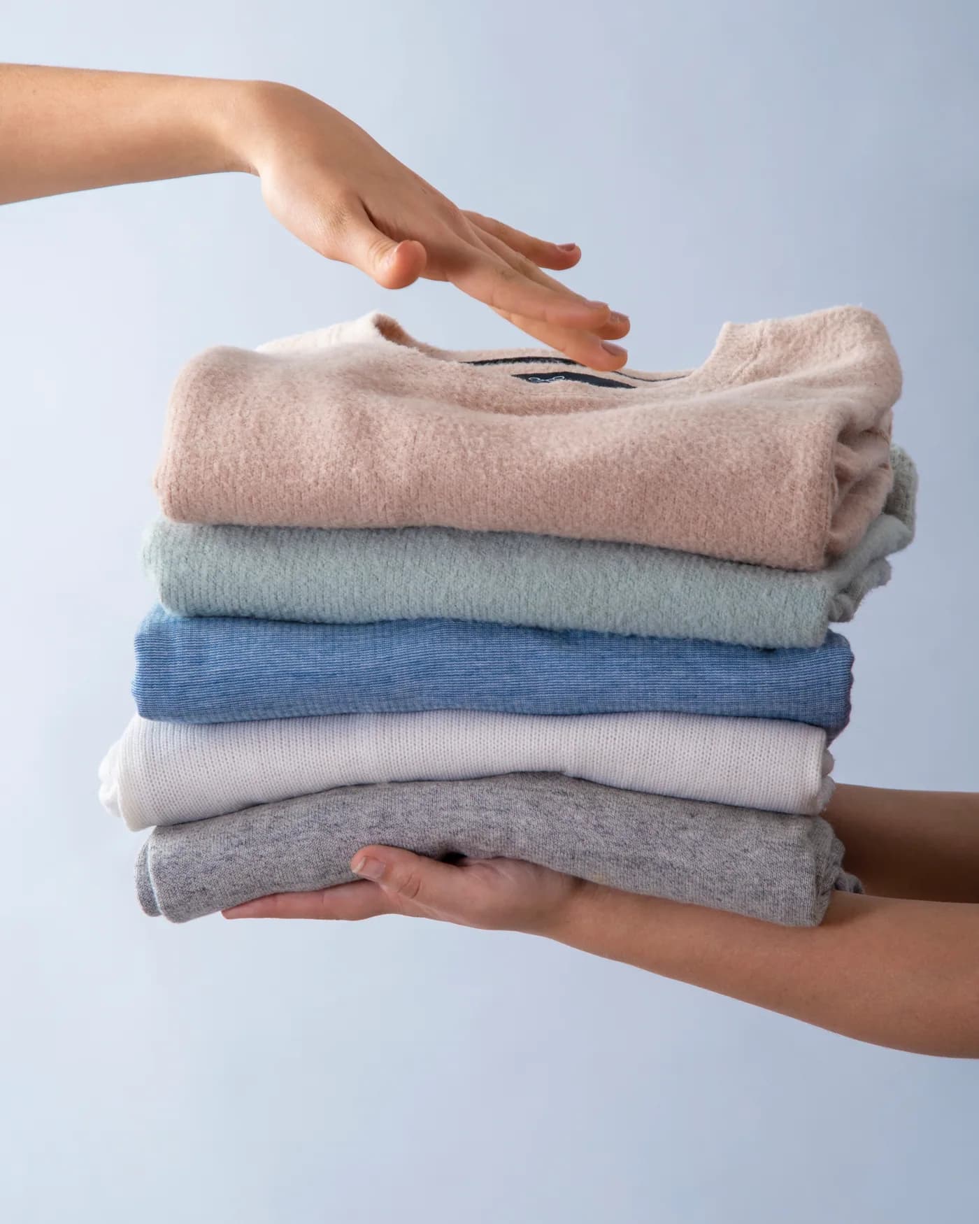 A folded stack of clean jumpers and shirts held in two hands